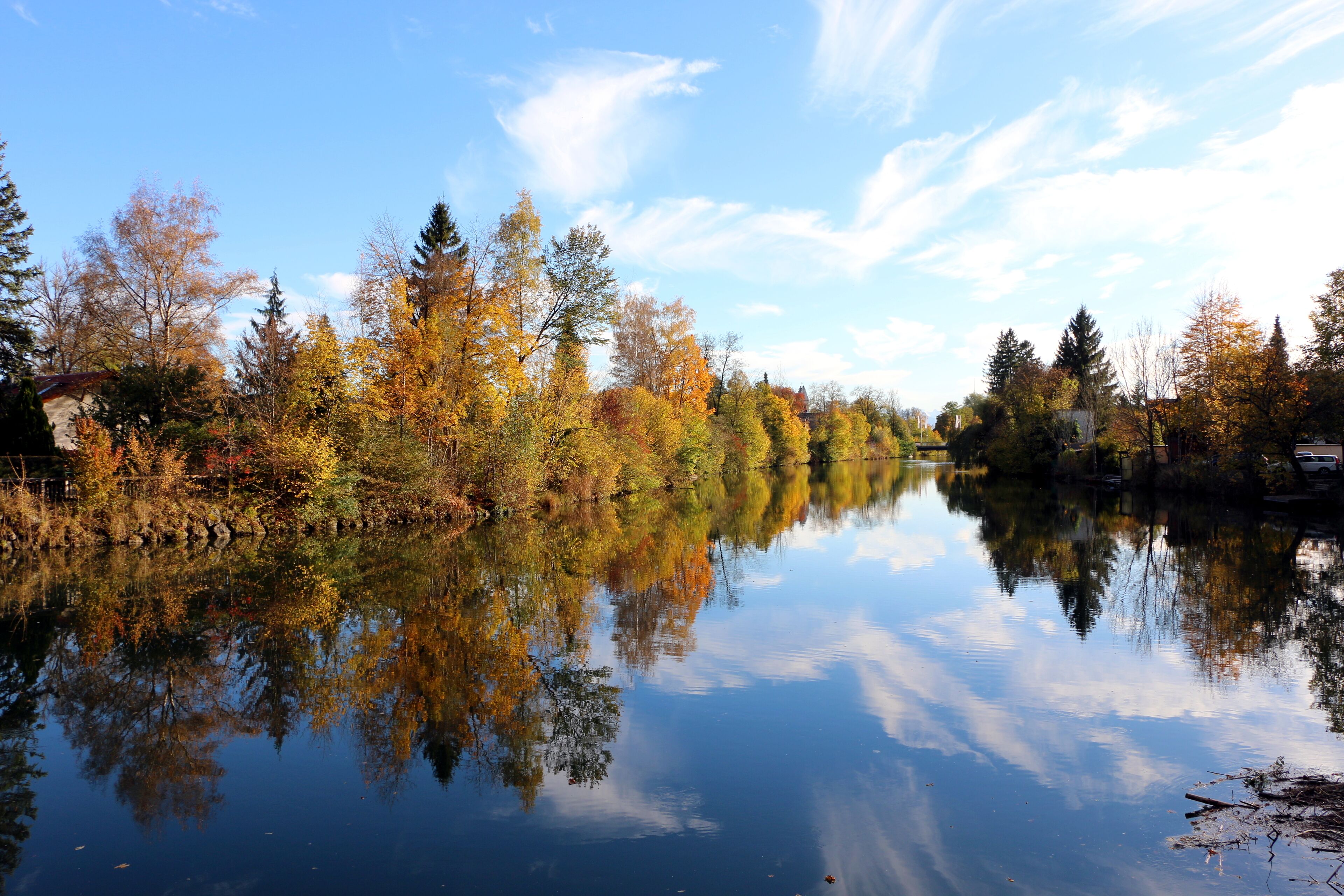 A calm river reflecting autumn trees and a clear sky.