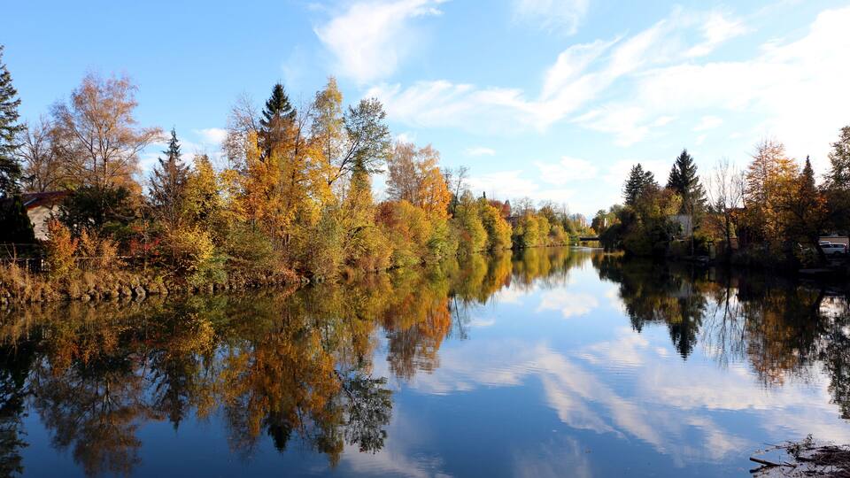 A calm river reflecting autumn trees and a clear sky.