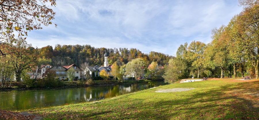 Un tranquilo pueblo junto al lago, con casas, una iglesia y follaje otoñal.