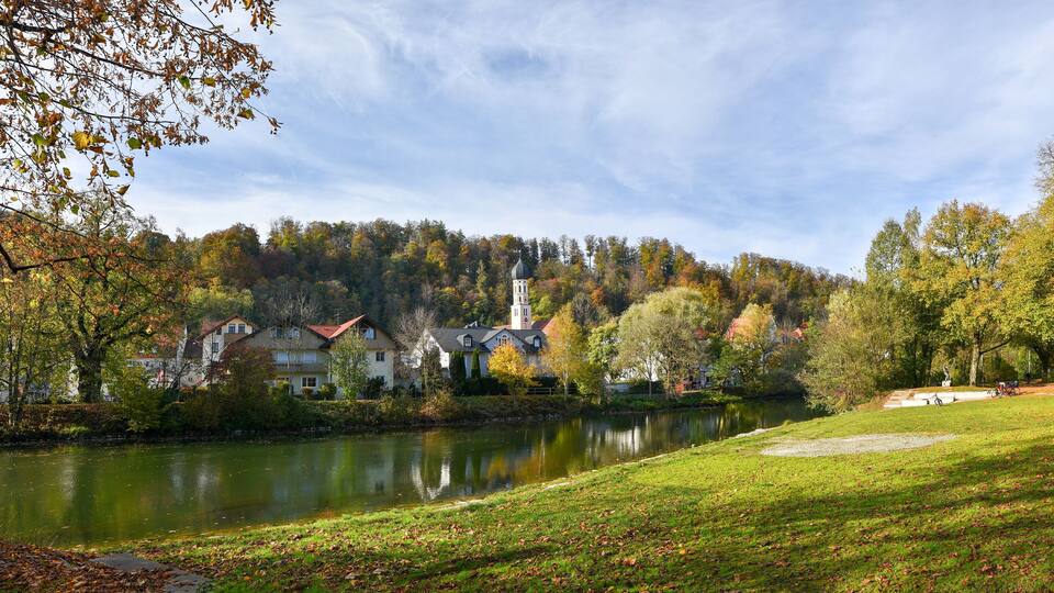 A serene lakeside town with houses, a church, and autumn foliage.