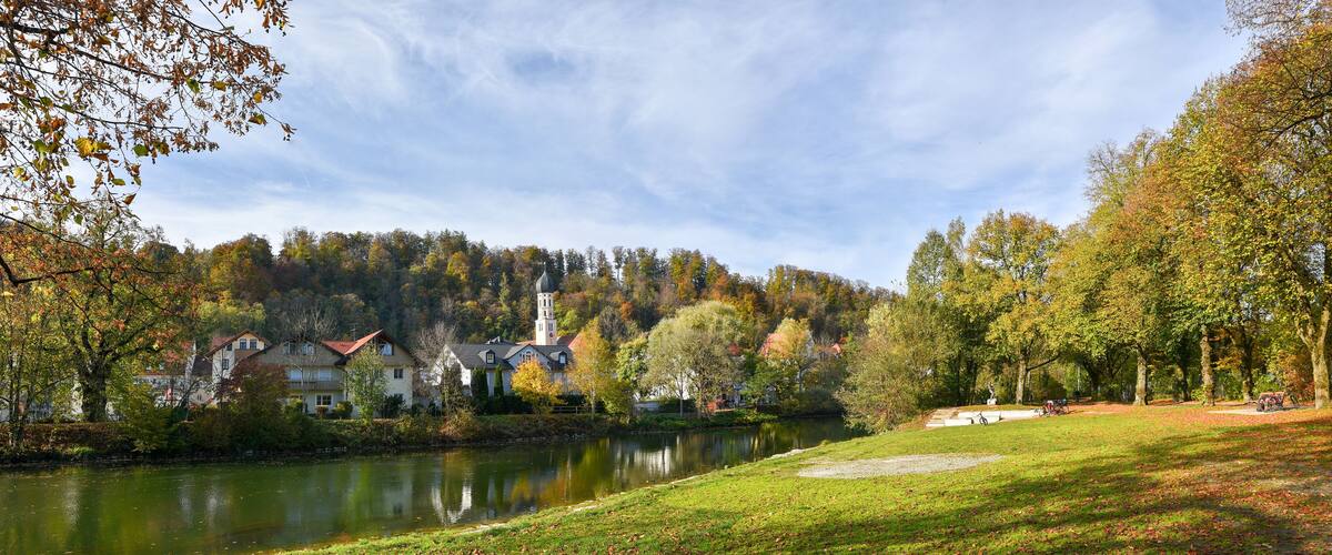 A serene lakeside town with houses, a church, and autumn foliage.