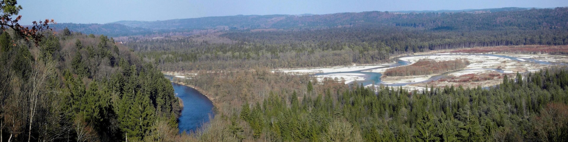 A river winding through a forested valley with a backdrop of distant hills.