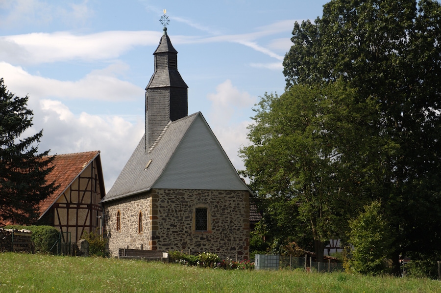 A stone church with a pointed steeple and a traditional timber-framed building nearby.
