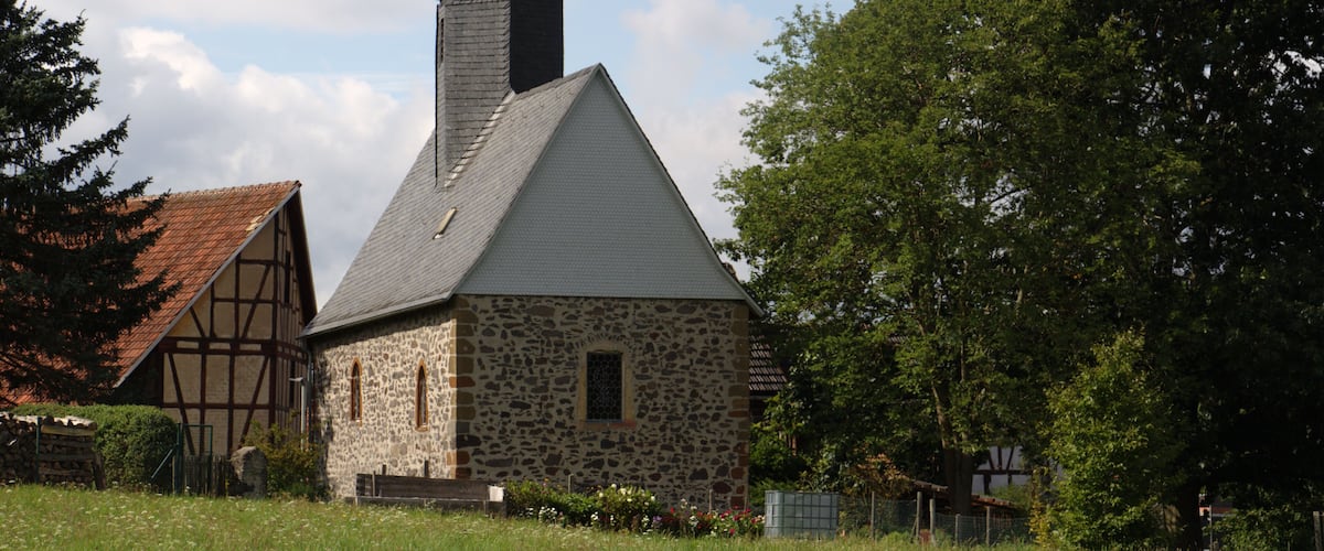 A stone church with a pointed steeple and a traditional timber-framed building nearby.
