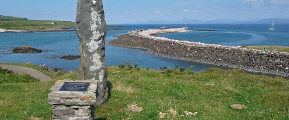 Eigg memorial stone. The 60 million year old lava pillar commemorates the island's historic buy-out in 1997 by the islanders and their partners in the Isle of Eigg Heritage Trust. In the background is the new pier where the CalMac ferry calls.