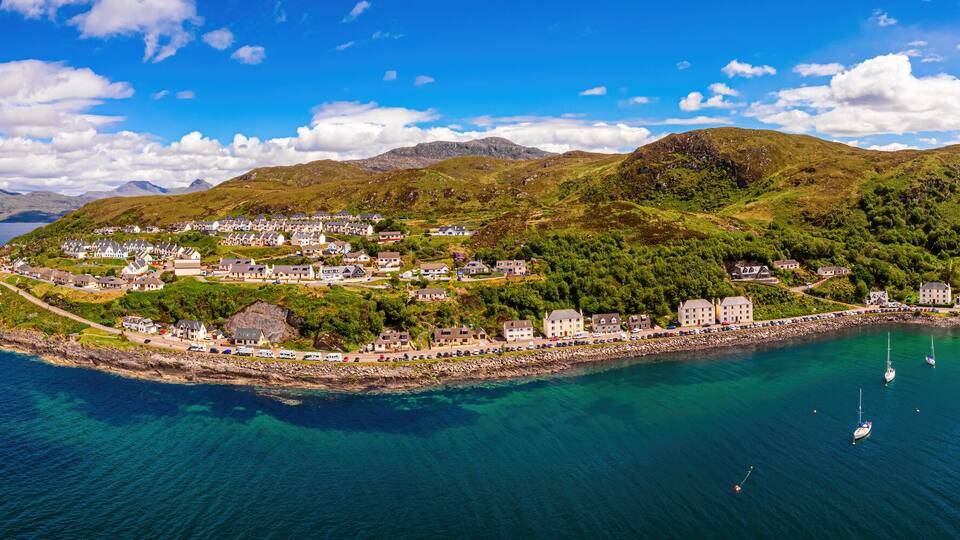 A coastal town with a harbor, boats, and a mountainous backdrop.