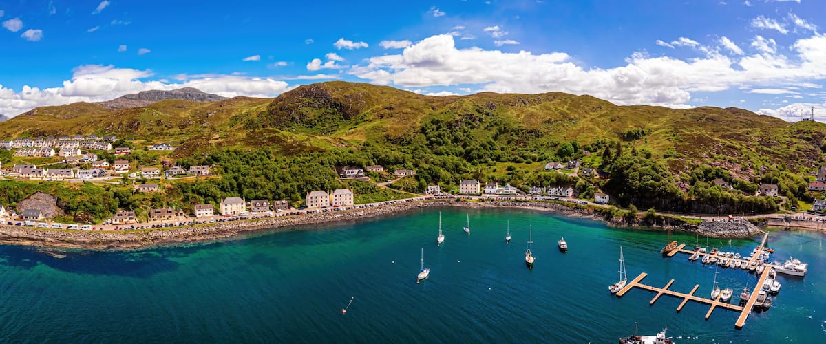 A coastal town with a harbor, boats, and a mountainous backdrop.