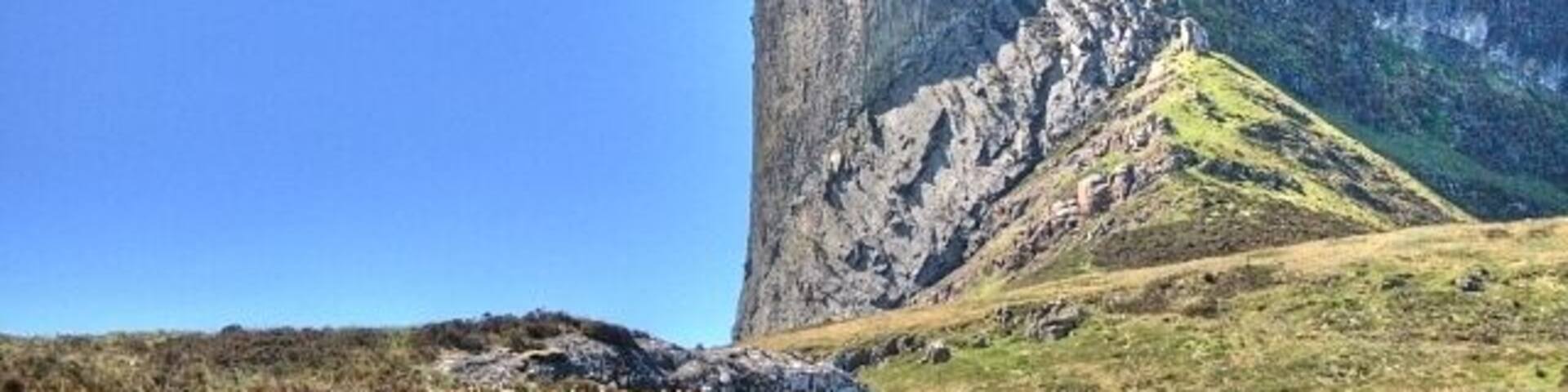 A large rock formation with a steep cliff and a clear blue sky.