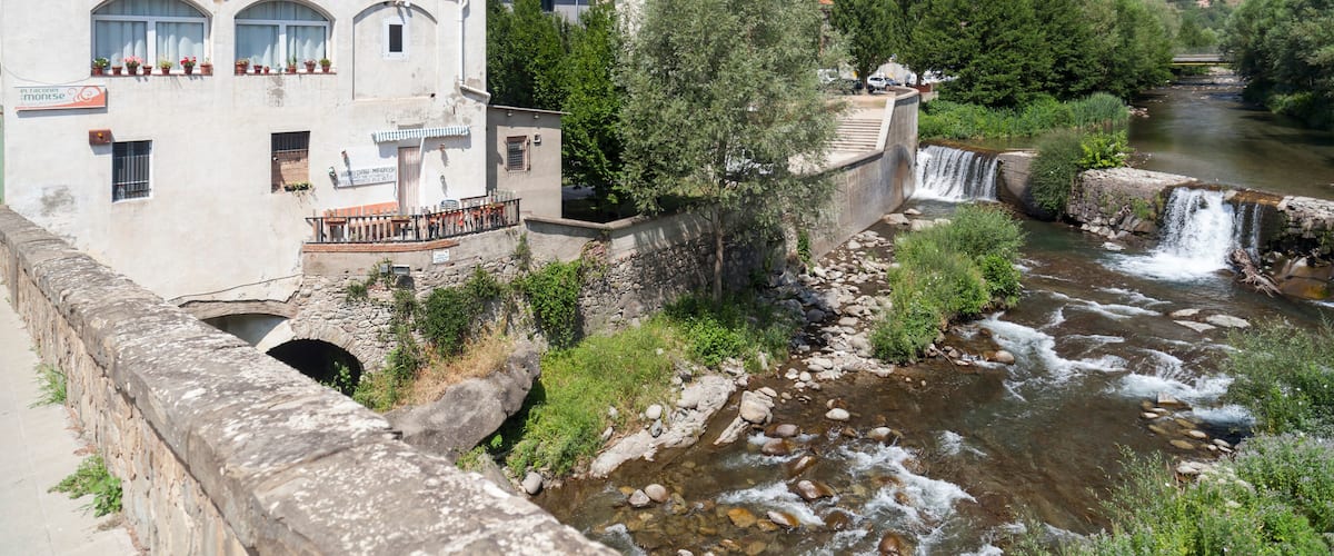 A river flowing through a town with a stone bridge and a building with arched windows.