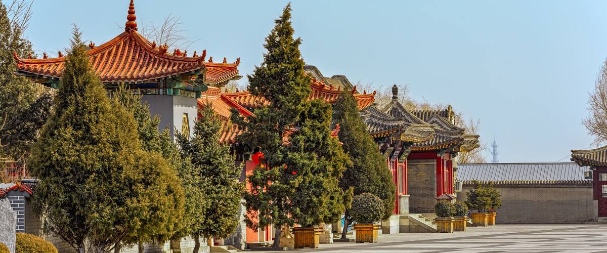 Arquitectura china tradicional con techos ornamentados y árboles en macetas en un patio.