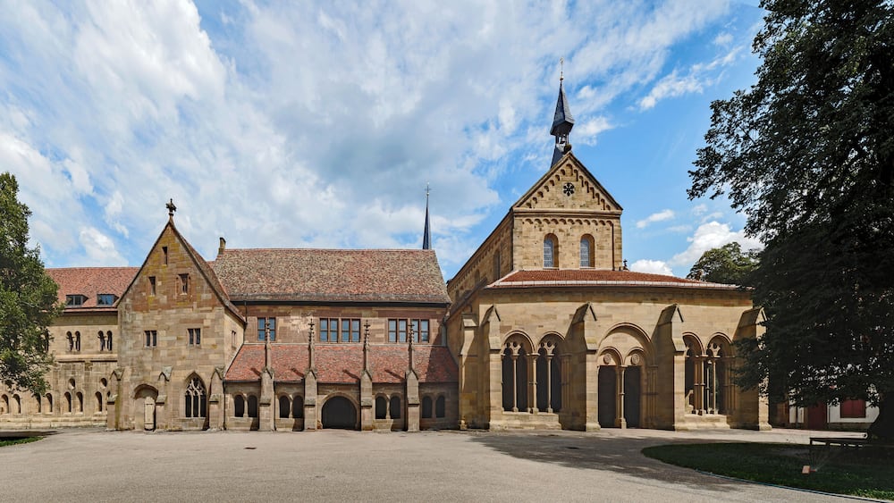 Ein historisches Gebäude mit einem großen Innenhof, einer Kirche mit spitzem Kirchturm und Rundbogenfenstern.