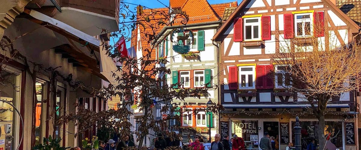 A cobblestone street lined with colorful half-timbered buildings, a Christmas tree, and people walking.
