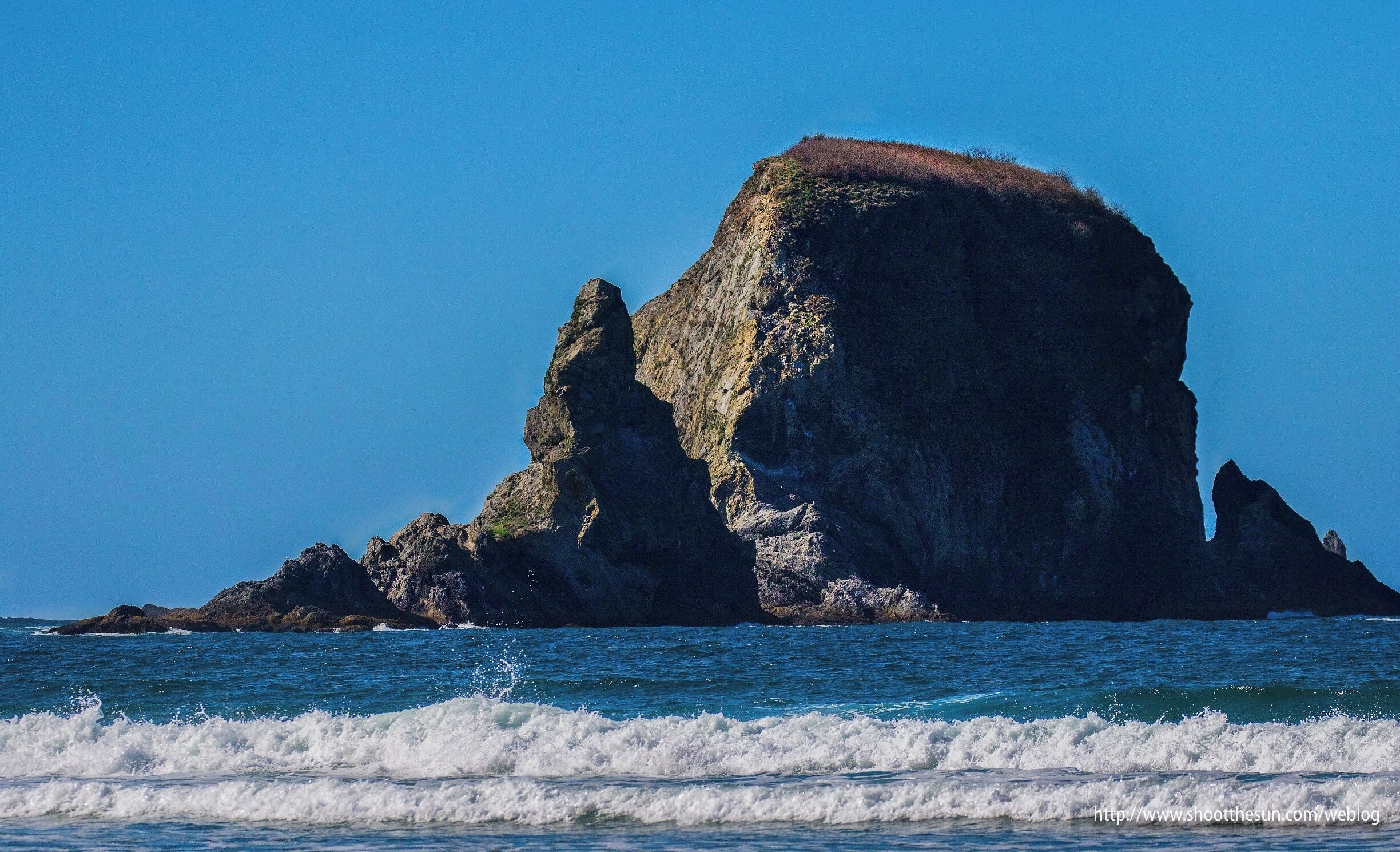 A rocky coastline with a prominent cliff and waves crashing against it.