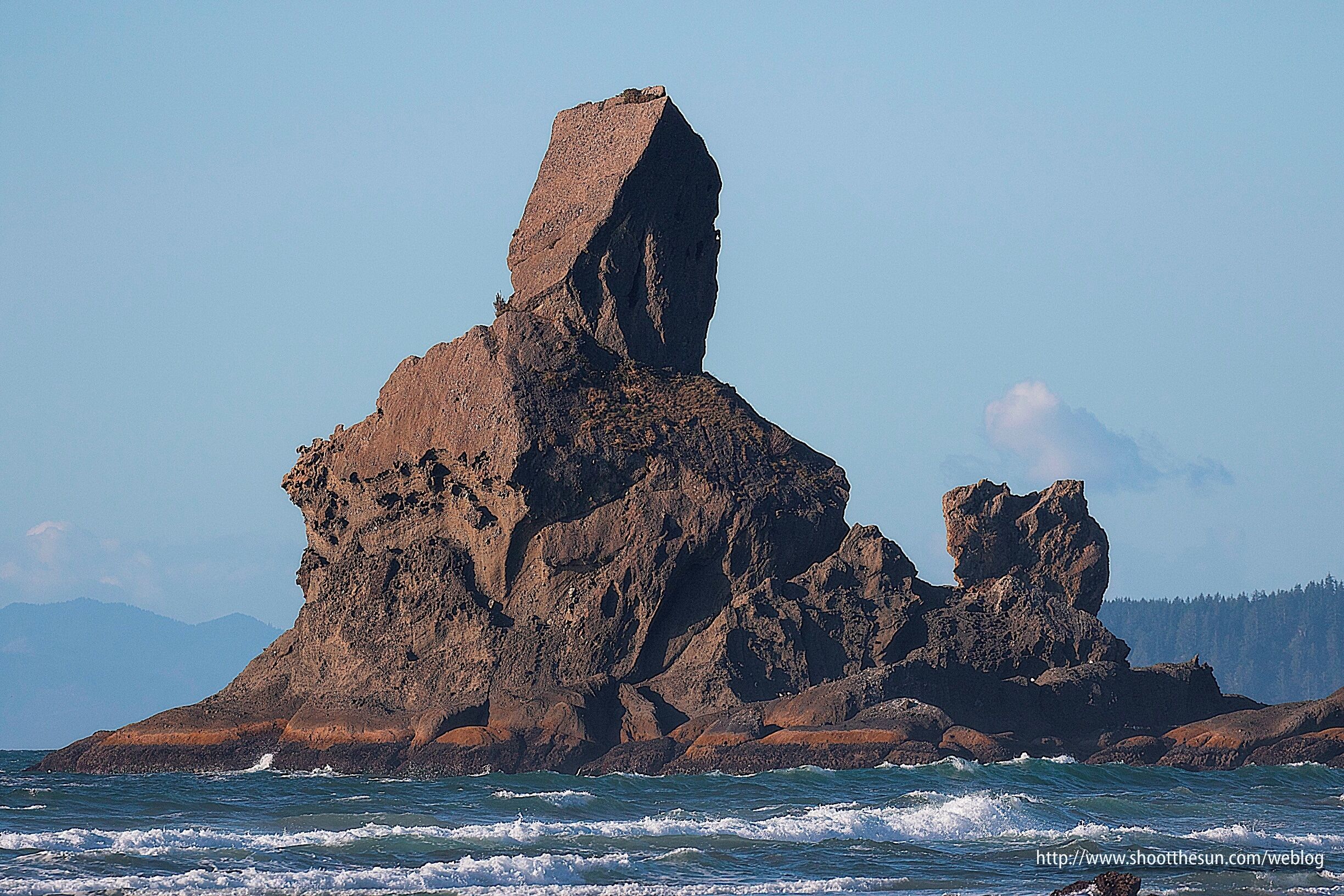 A rugged coastal rock formation with a prominent vertical pillar and smaller surrounding rocks.