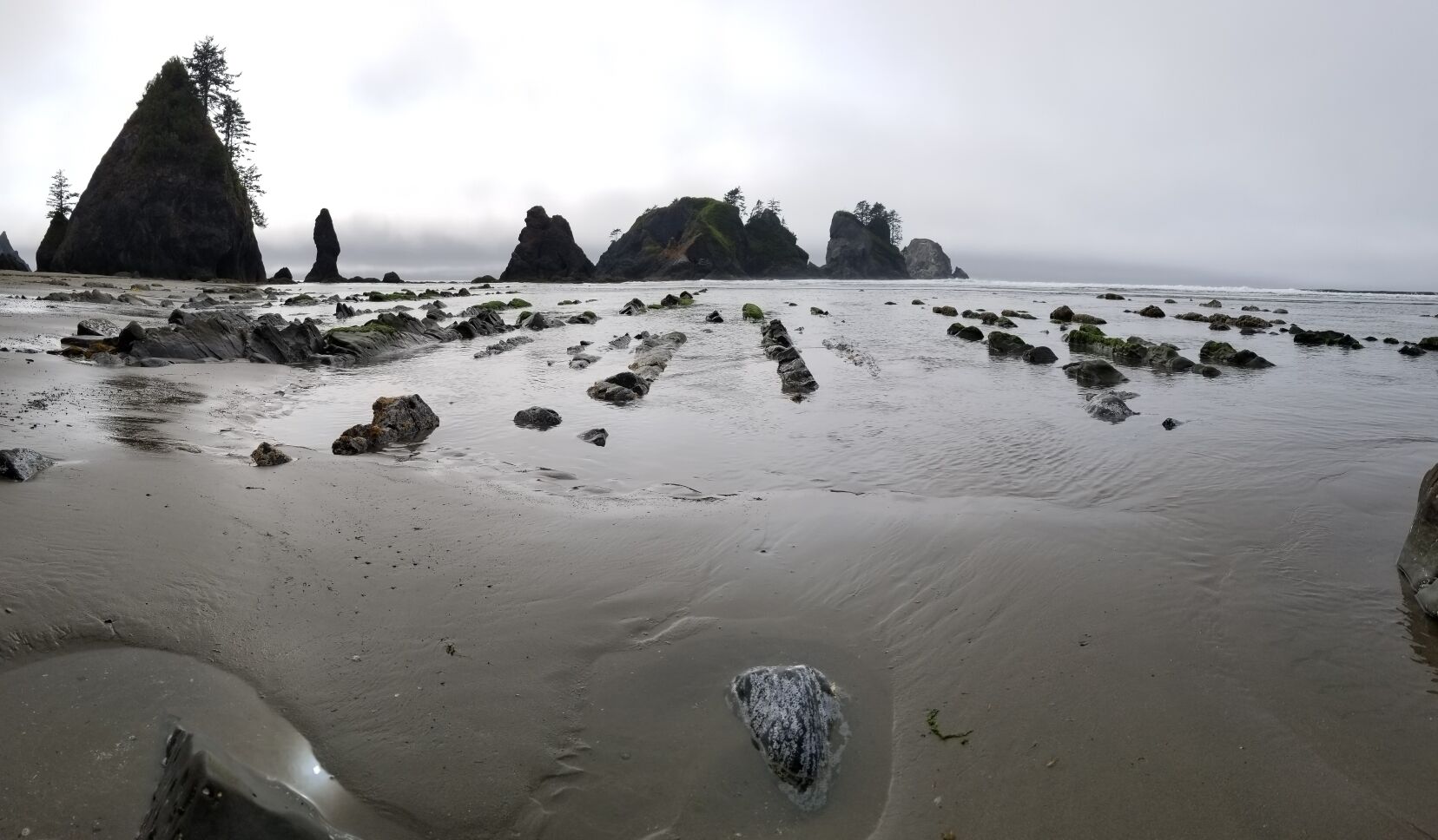 A rocky beach with large boulders and a forested island in the background.