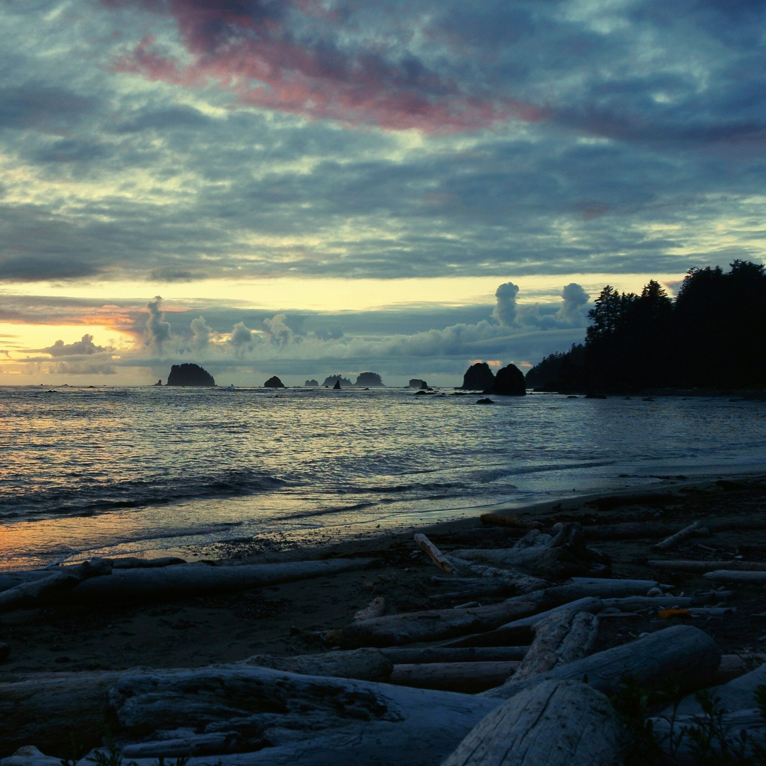 A coastal landscape with a beach, scattered rocks, and a sunset over the water.