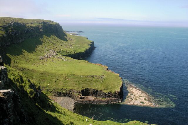 A coastal cliff with grassy areas and a rocky shoreline.