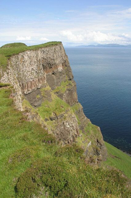 A steep cliff with grassy areas and a vast ocean in the background.