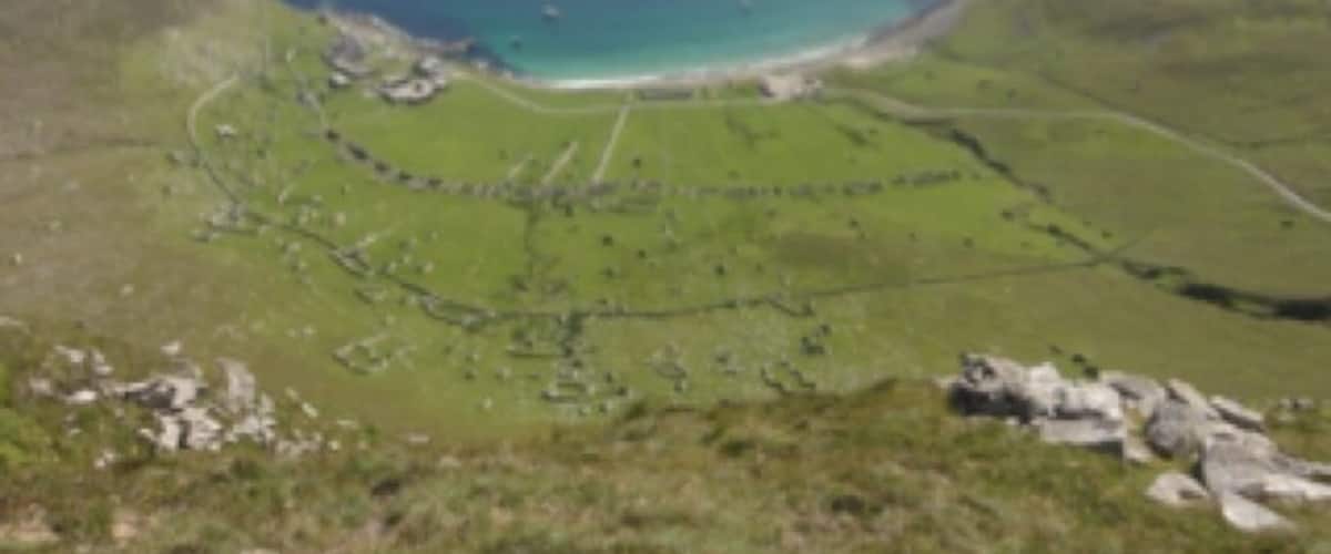 A coastal landscape with a bay, green hills, and a clear sky.