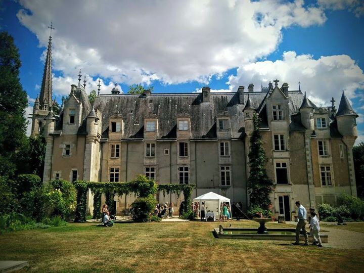 A large, historic building with multiple towers and a well-maintained garden in front.