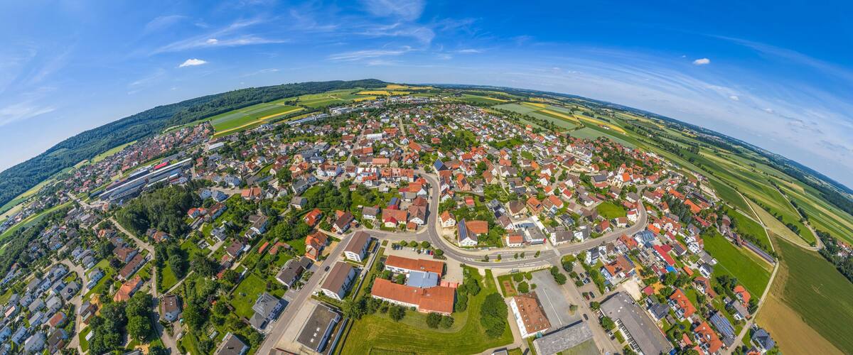 An aerial view of a town with red-roofed houses, green fields, and a railway track.
