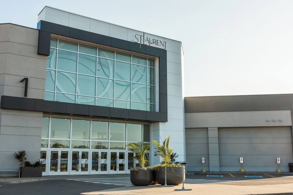 A modern building with a large glass facade, the name "STAURENT" above the entrance, and two large planters with plants in front.