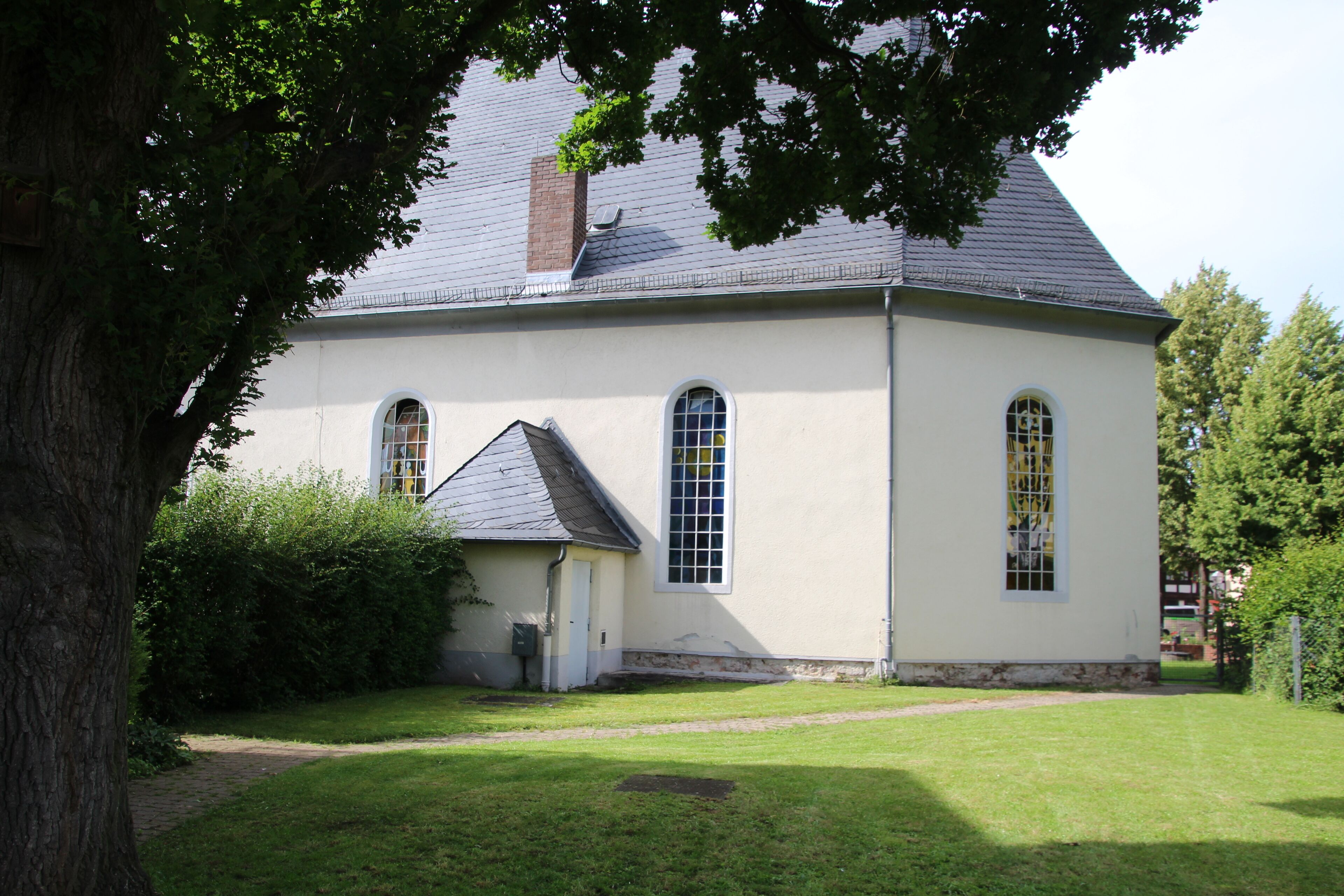 A white church with a grey roof, surrounded by a well-maintained lawn and trees.