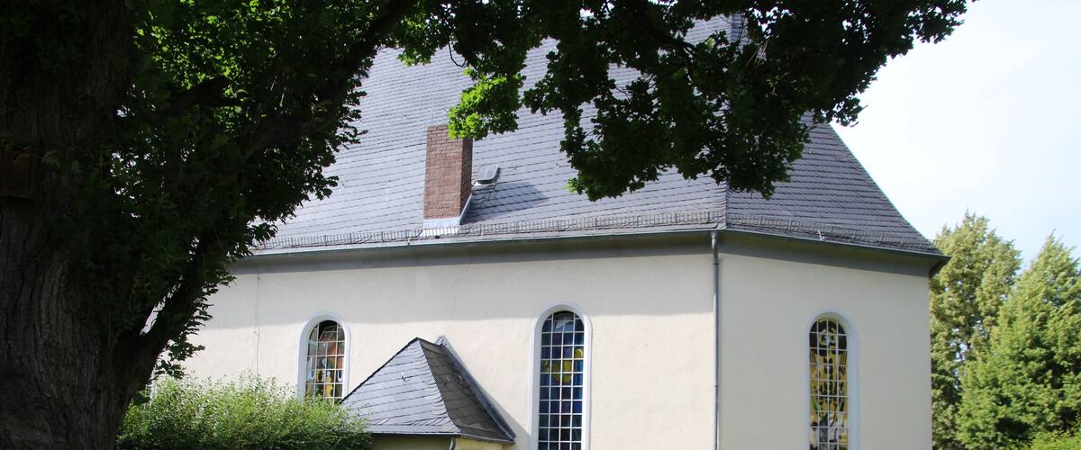 A white church with a grey roof, surrounded by a well-maintained lawn and trees.