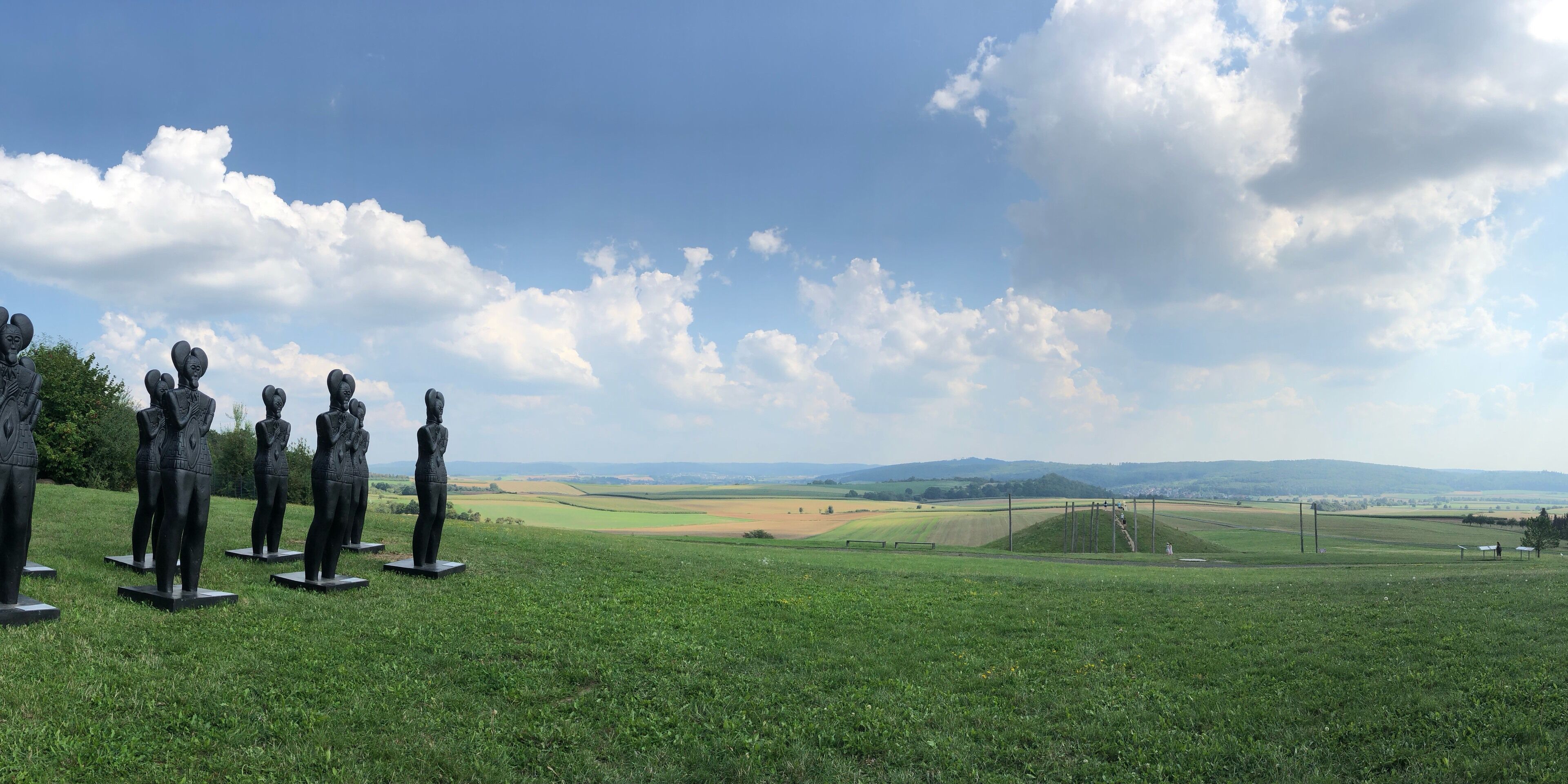 A grassy field with statues and a distant view of rolling hills and a clear sky.