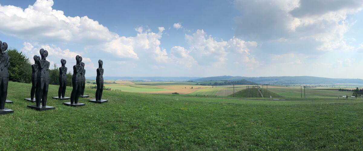 A grassy field with statues and a distant view of rolling hills and a clear sky.
