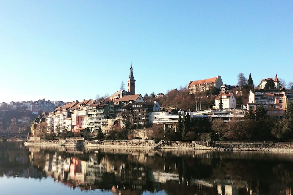 A calm river reflecting buildings and a church steeple.