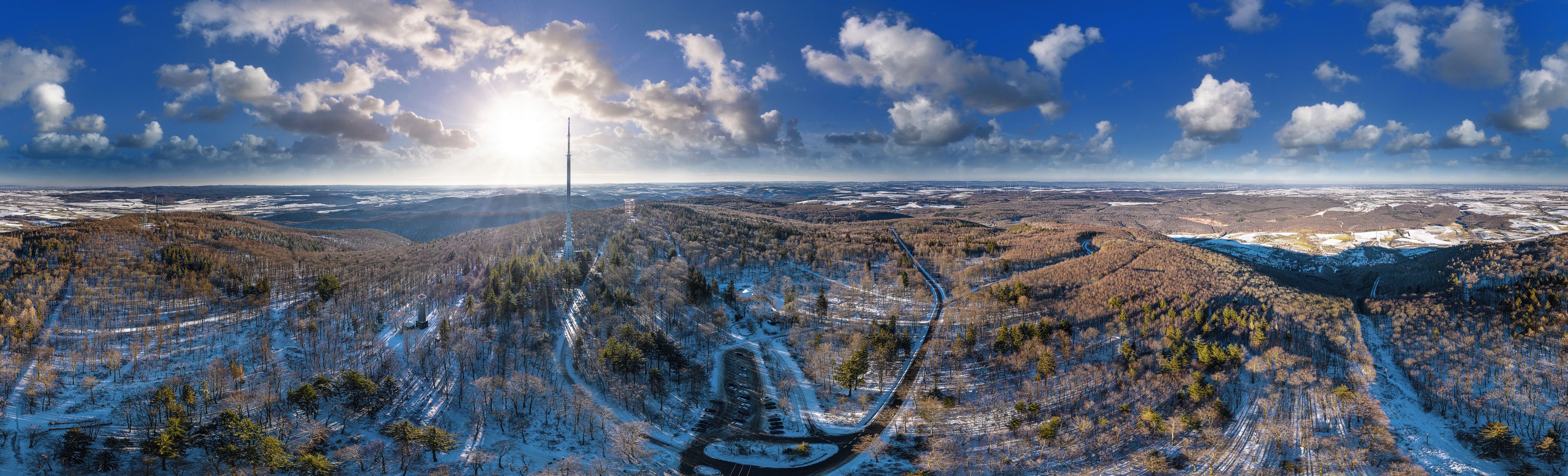 A panoramic view of a mountainous landscape with a clear sky, a prominent tower, and a winding road.