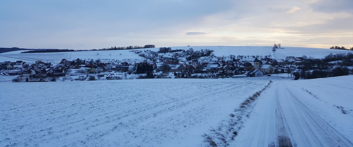 A snow-covered rural landscape with a village, fields, and a road.