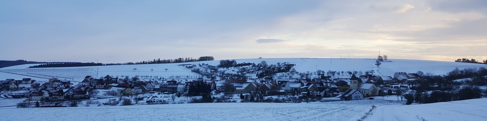 A snow-covered rural landscape with a village, fields, and a road.