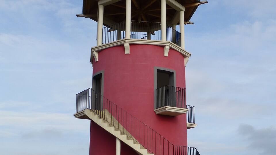 A red lighthouse with a white balcony and a black roof.