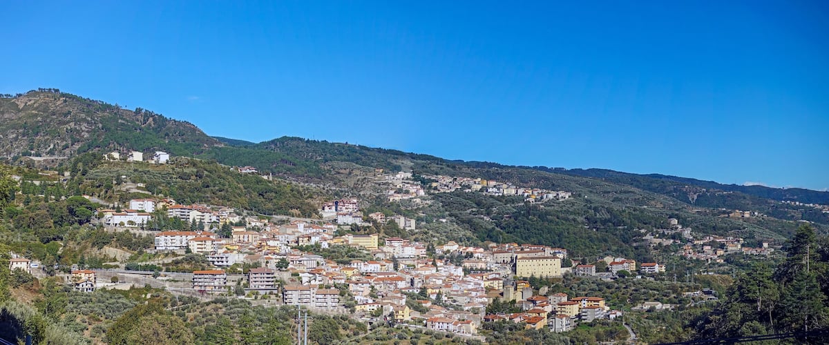 A hillside town with buildings nestled among trees and hills.
