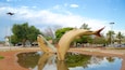 A large fish sculpture in a park with a pond reflecting the sculpture.