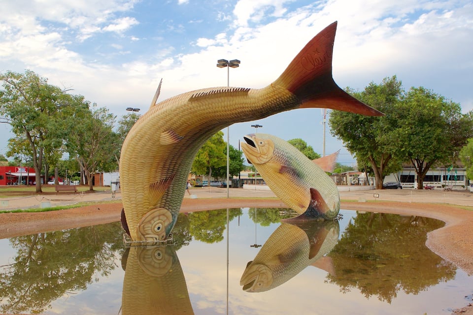 Uma grande escultura de peixe em um parque, com um lago refletindo a escultura.