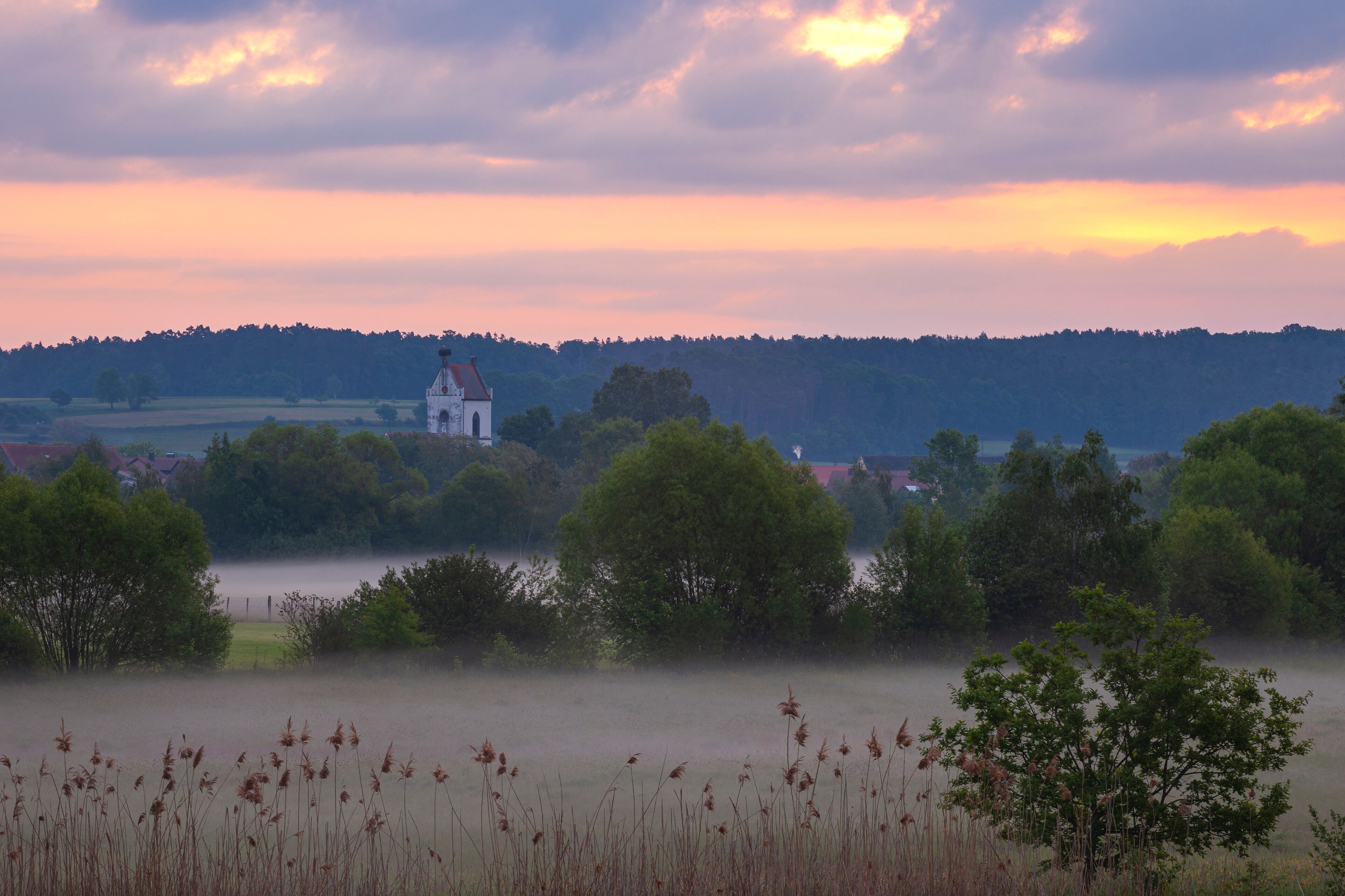 A church surrounded by trees and fields at sunset.