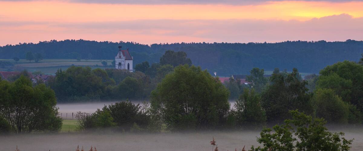 A church surrounded by trees and fields at sunset.