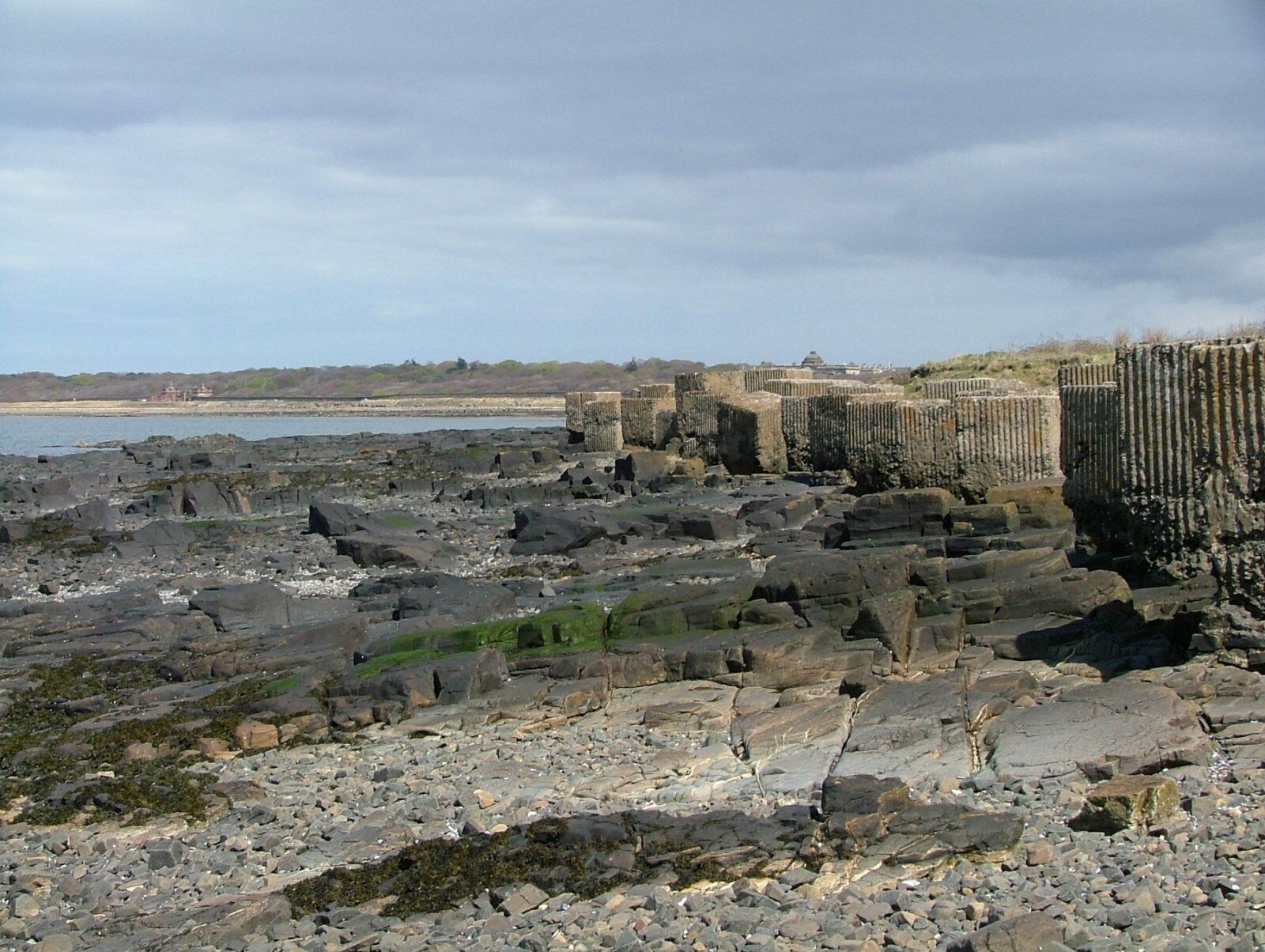 A rocky shoreline with ancient stone structures and a distant building.