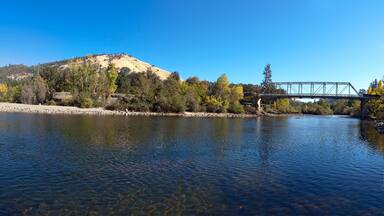 A river with clear water, a bridge, and a hill with trees.