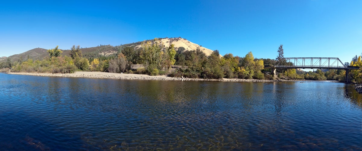 A river with clear water, a bridge, and a hill with trees.