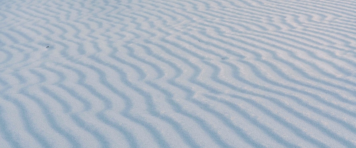 A vast white sand dune with rippled patterns and a clear sky with clouds.