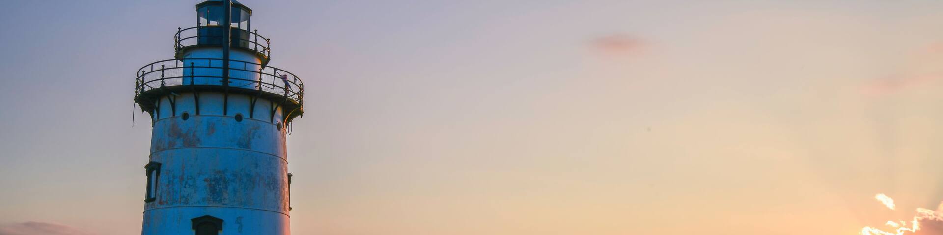A lighthouse on a rocky outcrop with a sunset in the background.