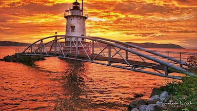Un phare avec un pont métallique enjambant une étendue d’eau, au coucher du soleil.