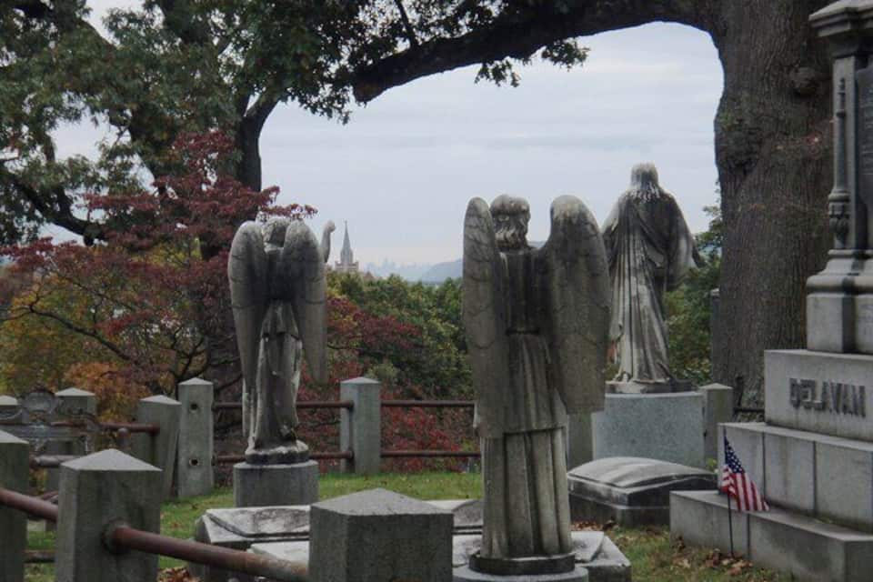 Ein Friedhof mit steinernen Statuen, einem großen Baum und einem entfernten Kirchturm.