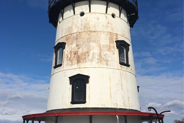A lighthouse with a white and red base, a black top, and a metal railing.