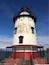 A lighthouse with a white and red base, a black top, and a metal railing.