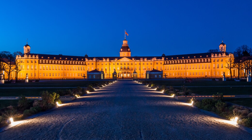 Un grand bâtiment illuminé, doté d’un dôme central et de deux tours, entouré d’un jardin symétrique agrémenté de sentiers.